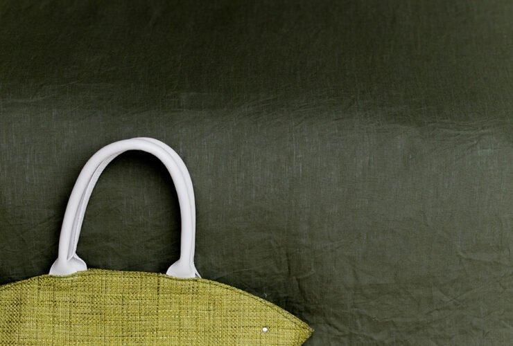 Green woven tote bag with white handles on a bench and a plate with sliced honeydew melon beside it.