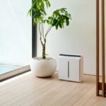 A modern air purifier beside an indoor plant in a minimalist home interior.