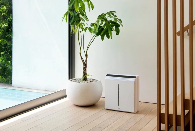 A modern air purifier beside an indoor plant in a minimalist home interior.