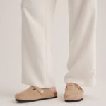 Person wearing white pants and beige slip-on clogs with a single button detail on the side.