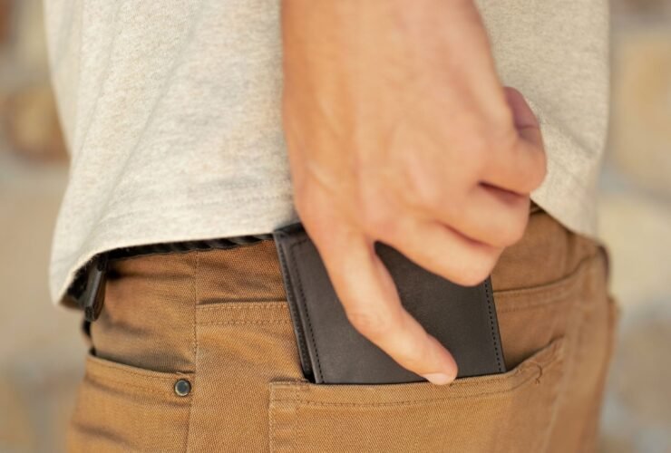 A person inserts a black wallet into the back pocket of brown pants.