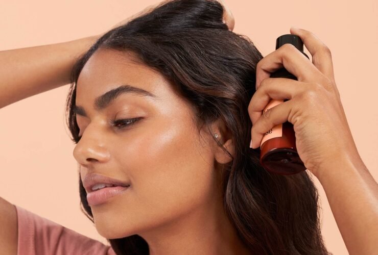 A person with their eyes closed applies a hair product from a bottle to their hair.