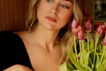 A person in a black shirt sits beside a vase of tulips.