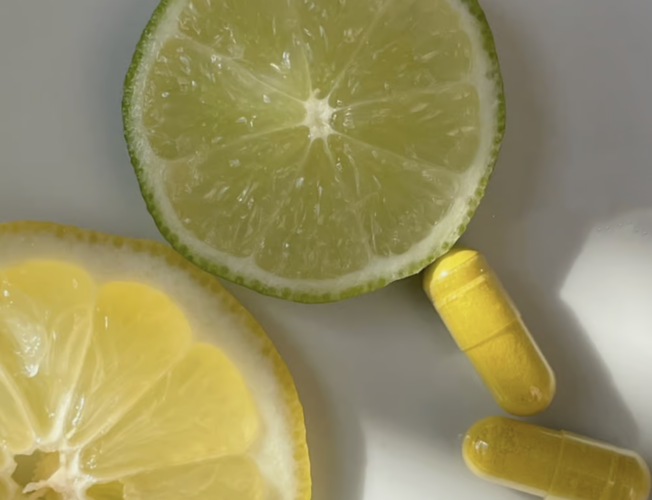 Two lemon slices, one green and one yellow, are placed next to three yellow capsules on a white surface.
