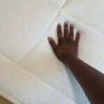 A hand with rings pressing down on a textured white mattress.