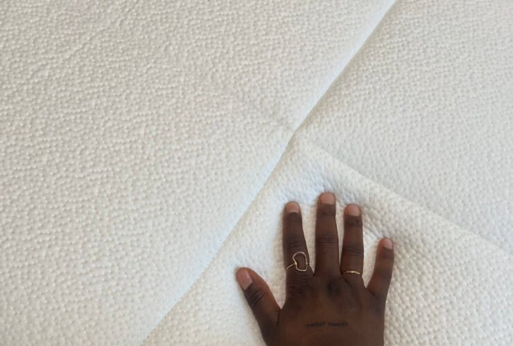 A hand with rings pressing down on a textured white mattress.