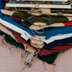 A stack of various colored clothes neatly hung on wooden and metal hangers, placed on a pink textured surface.