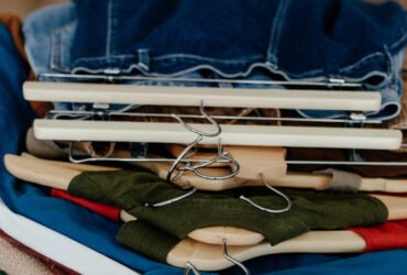 A stack of various colored clothes neatly hung on wooden and metal hangers, placed on a pink textured surface.